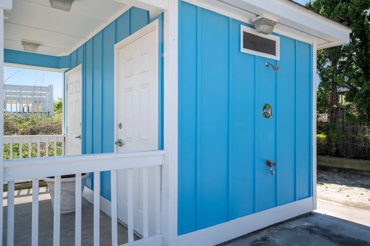 A bright blue exterior wall with white doors houses a convenient outdoor shower, perfectly suited for rinsing off sandy feet or beach gear after a visit to the shore. The cheerful atmosphere highlights practical features for easy transitions between beach and home life.