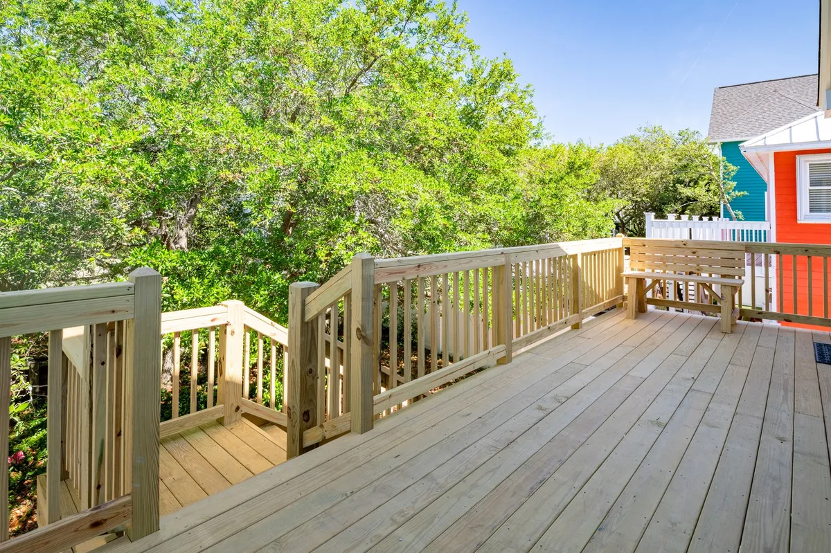 This cheerful exterior shot features a wooden deck bordered by trees and a colorful house in the background. The deck offers ample space for gatherings, morning coffee, or prepping for a day’s adventure in the surrounding nature.