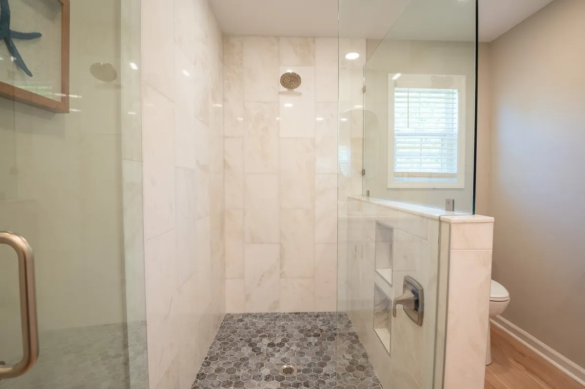 A modern bathroom showcasing a glass shower enclosure, hexagonal tile flooring, and framed artwork, evoking a tranquil, spa-like atmosphere.