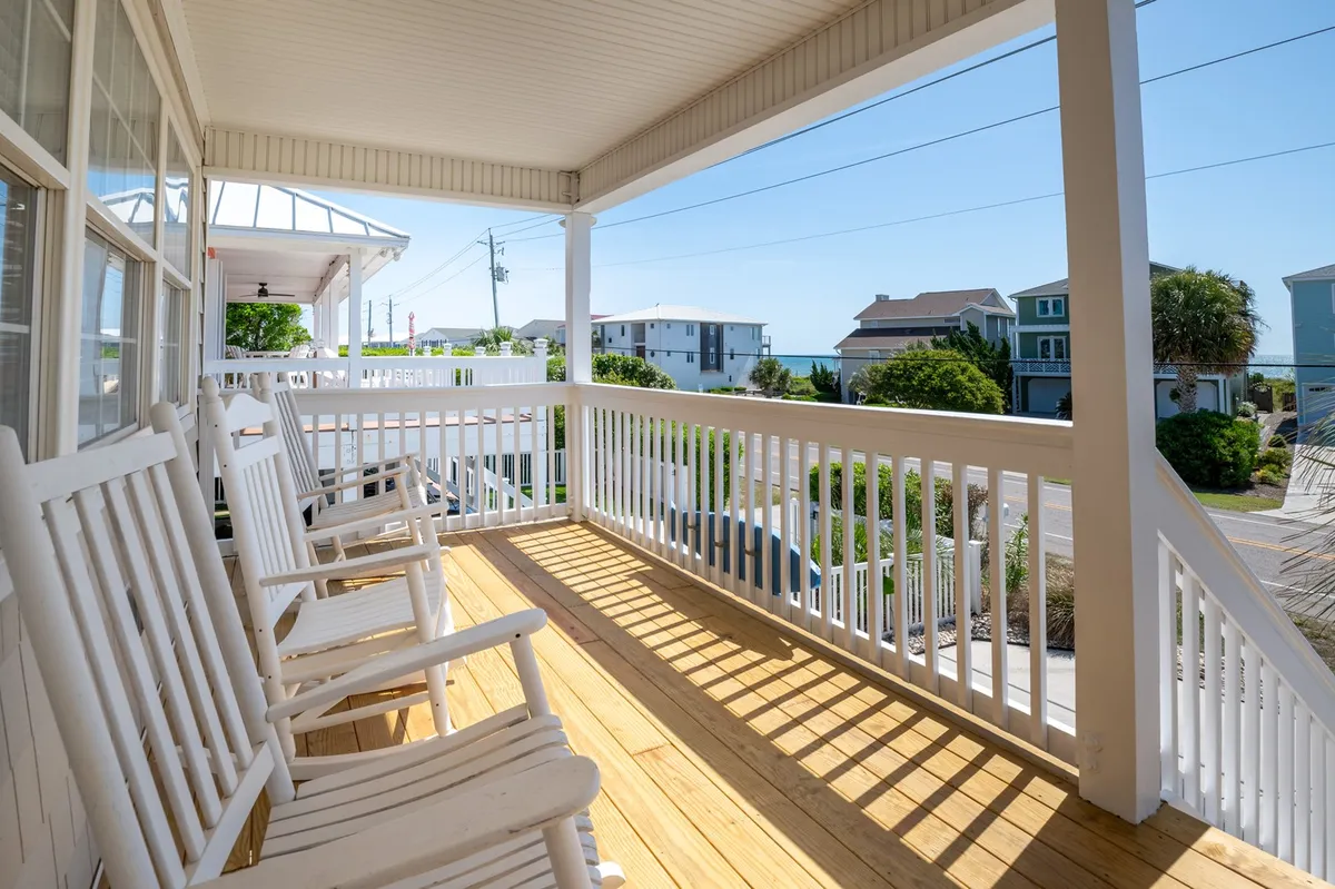 A balcony featuring classic rocking chairs and a view of the ocean beyond the railing. The tranquil scene is perfect for sipping coffee, unwinding, or enjoying the sunset, with a clear visual connection to the beach environment described in the section.