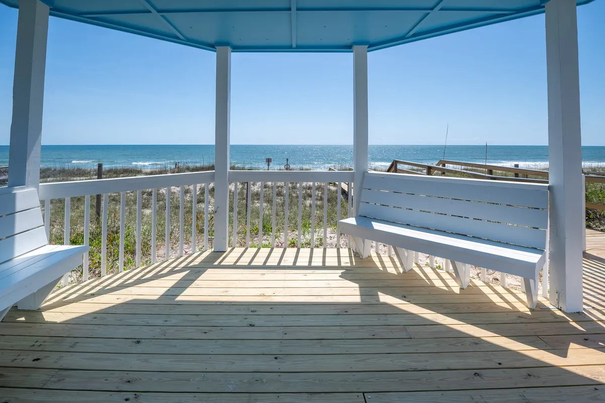 A peaceful exterior seating area with a wooden floor and an expansive view of the ocean. Comfortable chairs invite guests to relax, read, or watch dolphins swim; the space glows under the warm coastal light—ideal for enjoying sunsets after a refreshing rinse in the sand shower.
