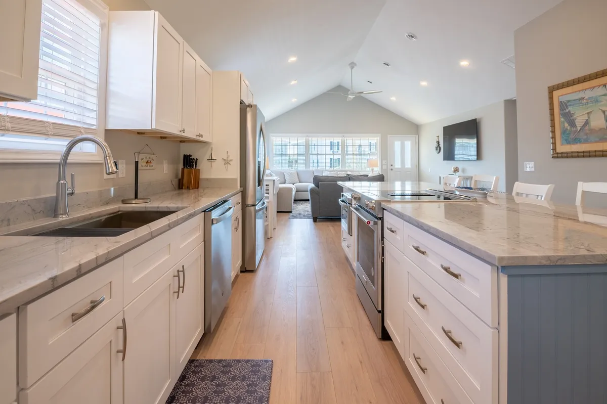 A bright, open-plan kitchen featuring a central island with a sleek sink, granite countertops, stainless steel appliances, and a window view that looks into the living area. The layout encourages socializing and family gatherings, with ample space for meal preparation and connection.