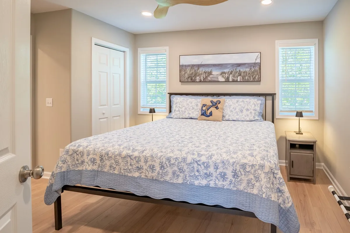 A serene bedroom featuring a large bed with blue floral bedding, framed artwork on the wall, and small bedside lamps. Soft natural light filters through the window, creating a calm and restful mood.