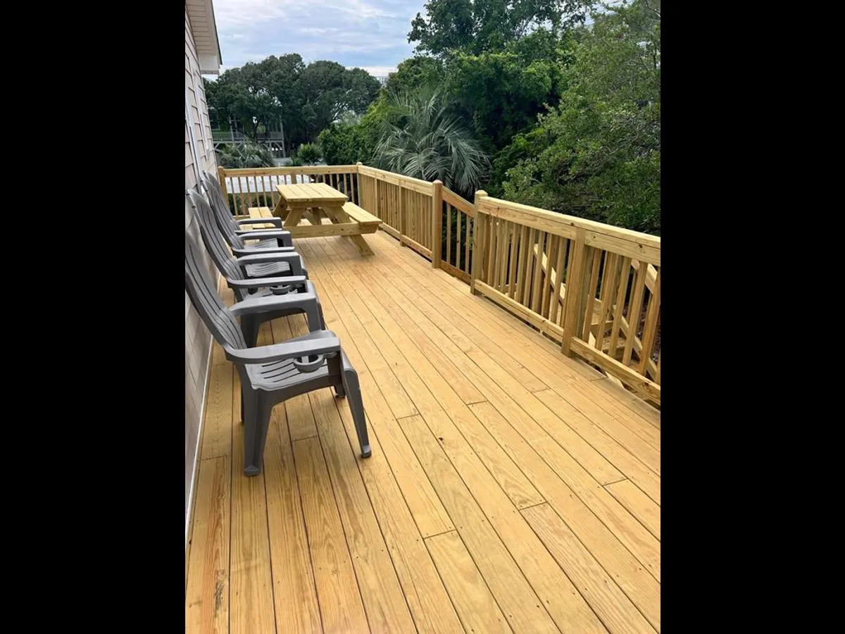 The image highlights a casual and inviting outdoor space with a wooden deck, picnic table, plastic chairs, and lush surrounding greenery. The area is perfect for outdoor dining, socializing, or simply basking in nature, with ample space for gear and flexible recreation.