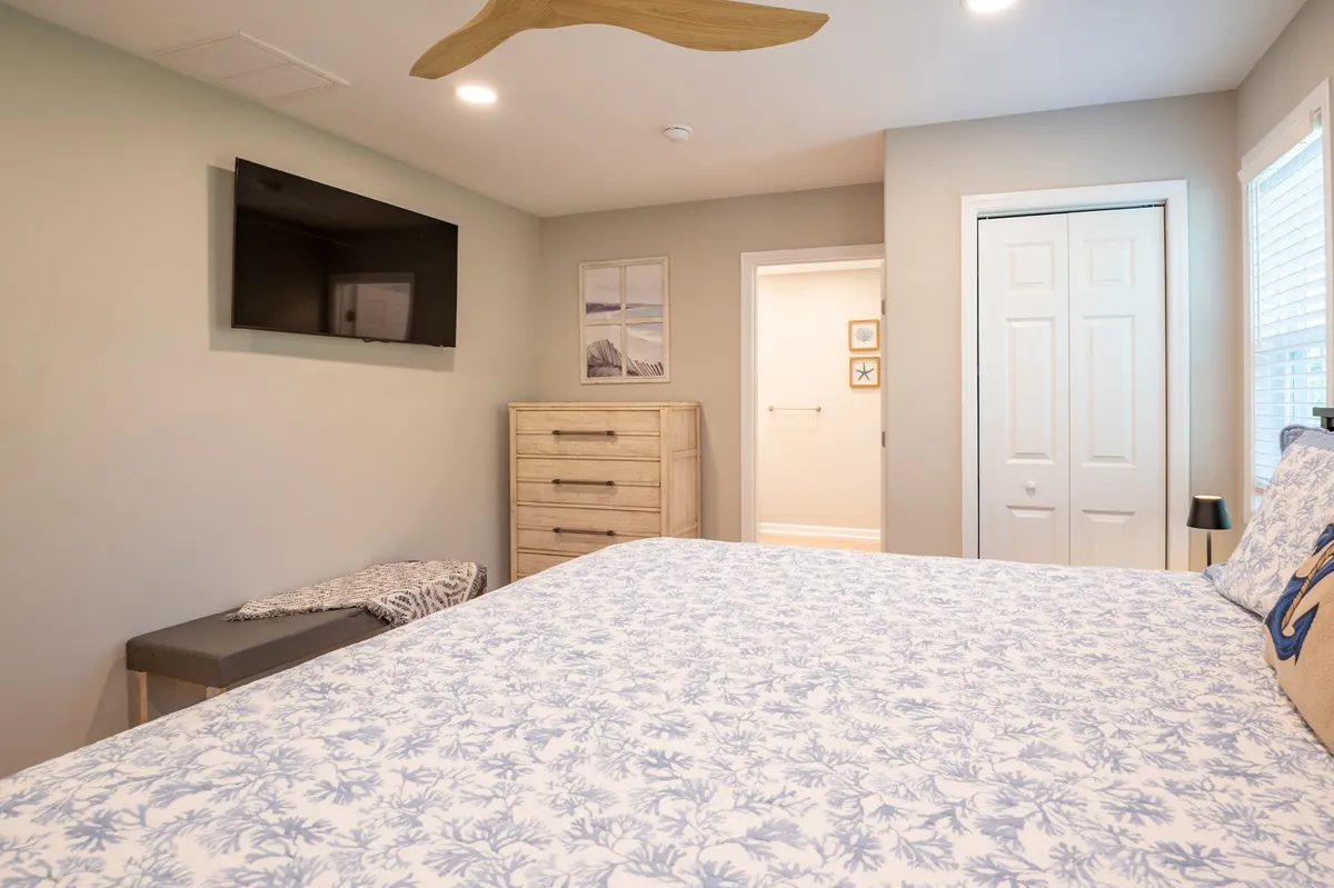 A cozy bedroom with floral bedding, a wall-mounted TV, dresser, and artwork. The setup is both functional and restful, letting guests relax with entertainment or unwind in peace.