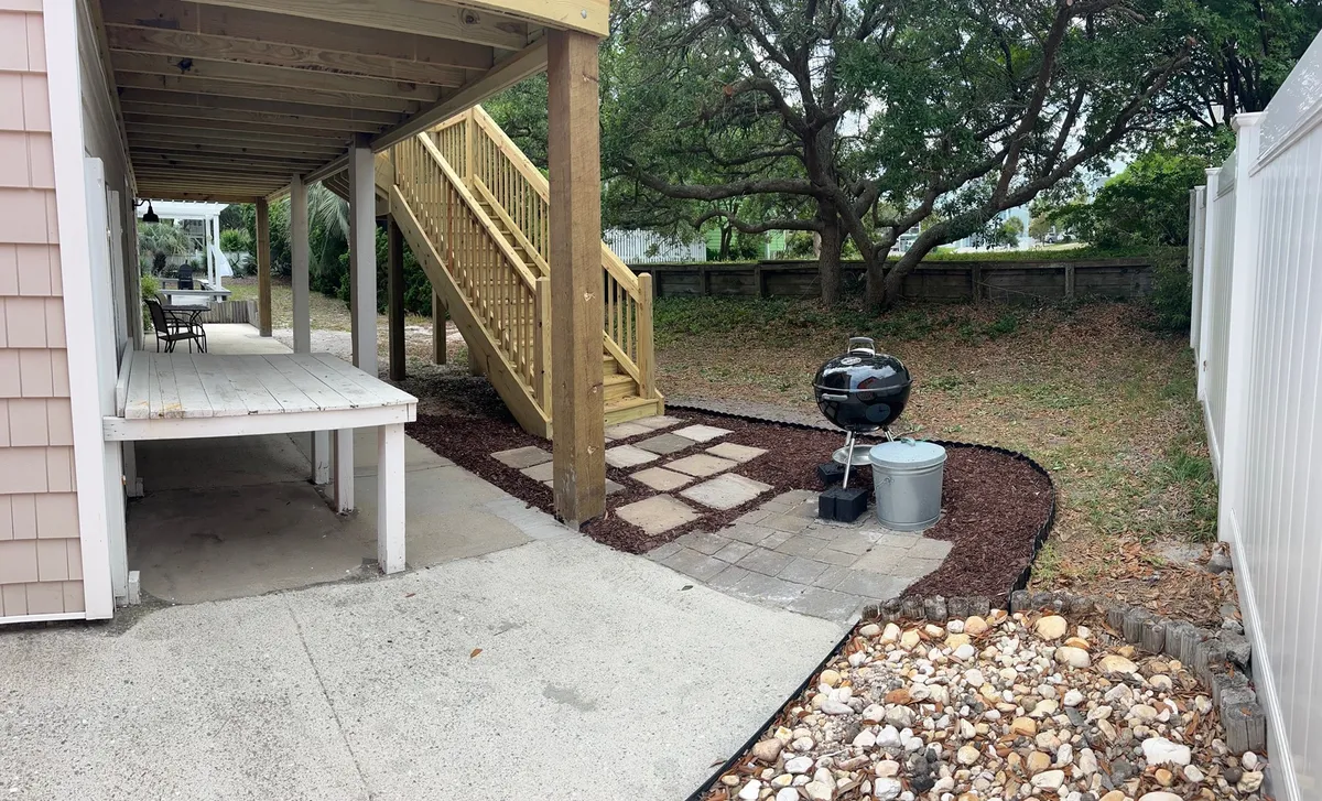 An outdoor space featuring a staircase leading to a patio with a grill and a table, surrounded by thoughtfully landscaped greenery. The scene is primed for barbecuing, alfresco dining, and relaxed family gatherings, evoking the feel of laid-back afternoons and memorable evening meals outdoors.