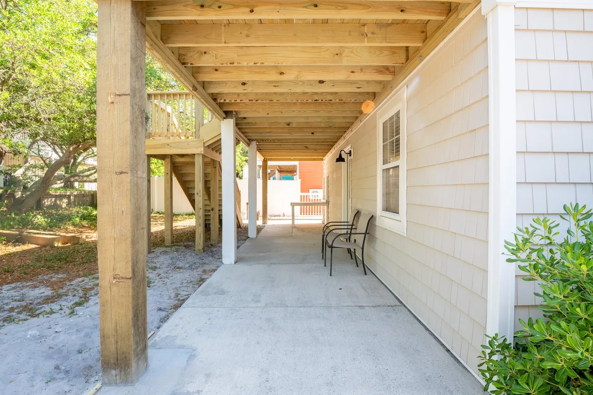 An inviting outdoor seating area with wooden beams, a concrete pathway, and landscaped greenery creates a relaxing environment for socializing and enjoying the fresh air. The scene suggests the transition from the comfort of the home to nearby attractions and the beach.