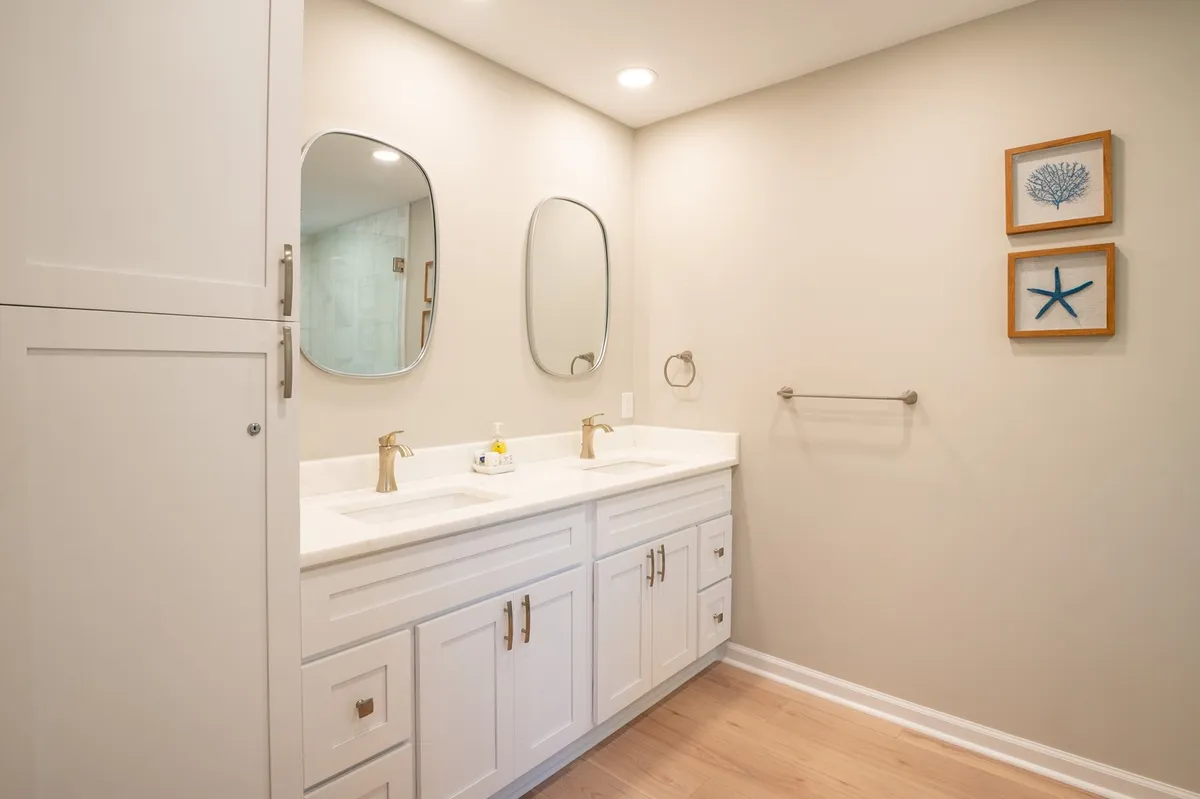 A contemporary bathroom with a dual sink vanity, mirrored cabinets, and decorative wall art. The space is light-filled and organized, ideal for morning or evening routines.